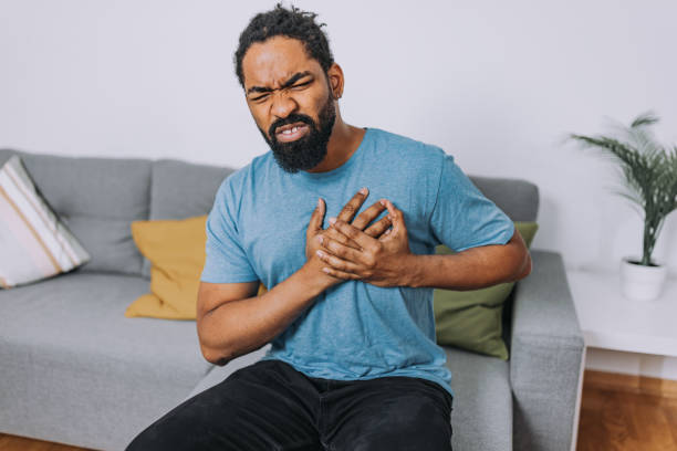 A mid-adult African-American man is holding his chest with a negative facial expression.