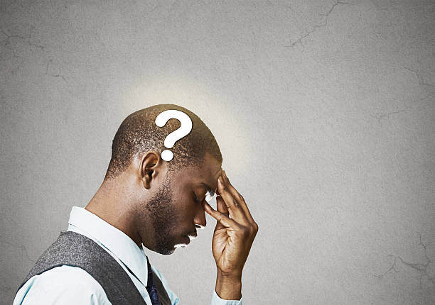 Side view portrait young puzzled business man thinking solving problem fingers on forehead looking down question mark over head isolated grey wall background copy space. Emotion expression perception